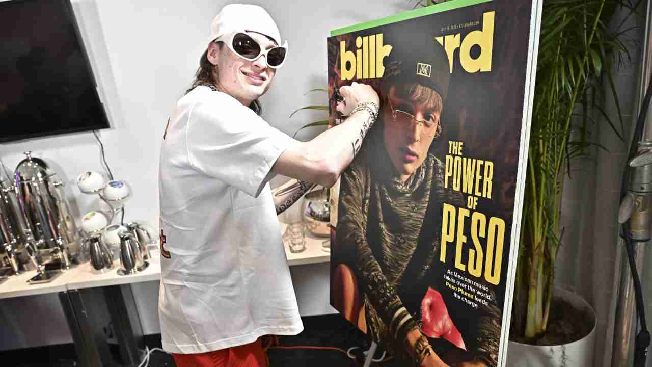 Peso Pluma mientras firma un cartel de Billboard